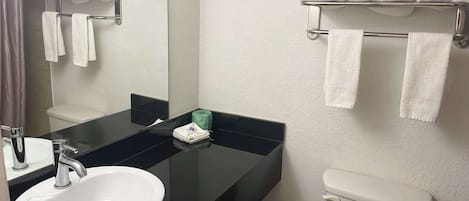 A bathroom with a white sink, a mirror, a black countertop, a toilet, and towel racks with white towels.