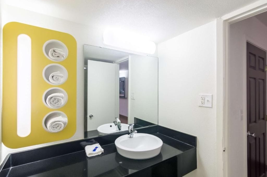 Un baño con lavamanos blanco, espejo y toallero amarillo con cuatro toallas.