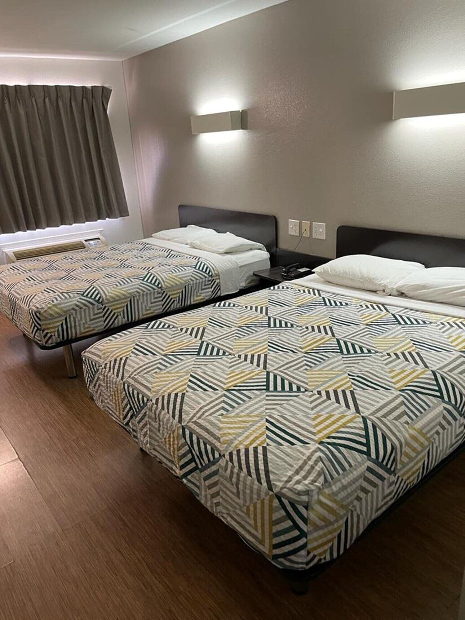 Una habitación de hotel con dos camas, una ventana con cortinas y una lámpara fijada a la pared.