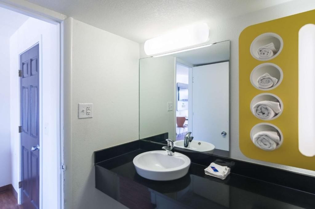 Casa de banho com lavatório branco, espelho e toalheiro amarelo.