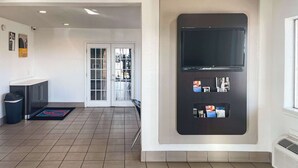 Eine Hotellobby mit einer Rezeption, einem Mülleimer, einer Tür zum Außenbereich und einem an der Wand befestigten Fernseher.