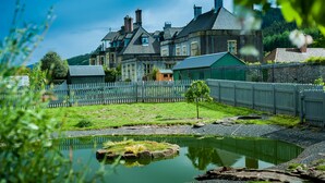 A traditional building with a stone facade, a small pond, and a white picket fence. - Llangoed Hall (Brecon)