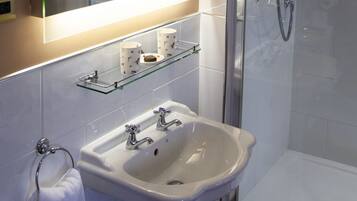 A bathroom with a glass-enclosed shower, a white sink with two faucets, and a mirror above the sink.