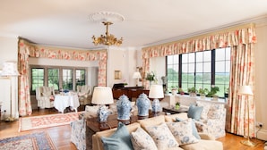 A spacious living room with a sofa set, a piano, and a large window with floral curtains.