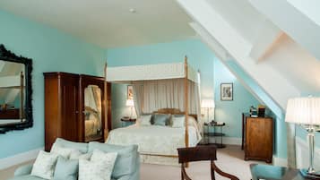 Quarto com cama de dossel, área de estar com sofá e poltrona, e armário de madeira.