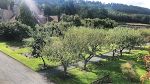 A landscaped garden with neatly trimmed grass, trees, and a stone building in the background.