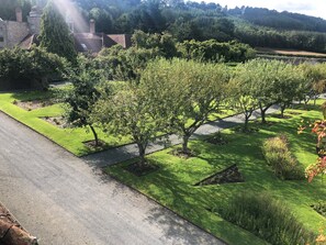 A landscaped garden with neatly trimmed grass, trees, and a stone building in the background.