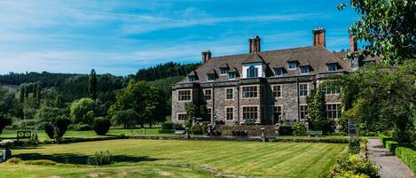 A large stone building with multiple chimneys, surrounded by a well-maintained lawn and trees.