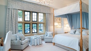 A four-poster bed, a sitting area with a table, and a view of a bridge through large windows.