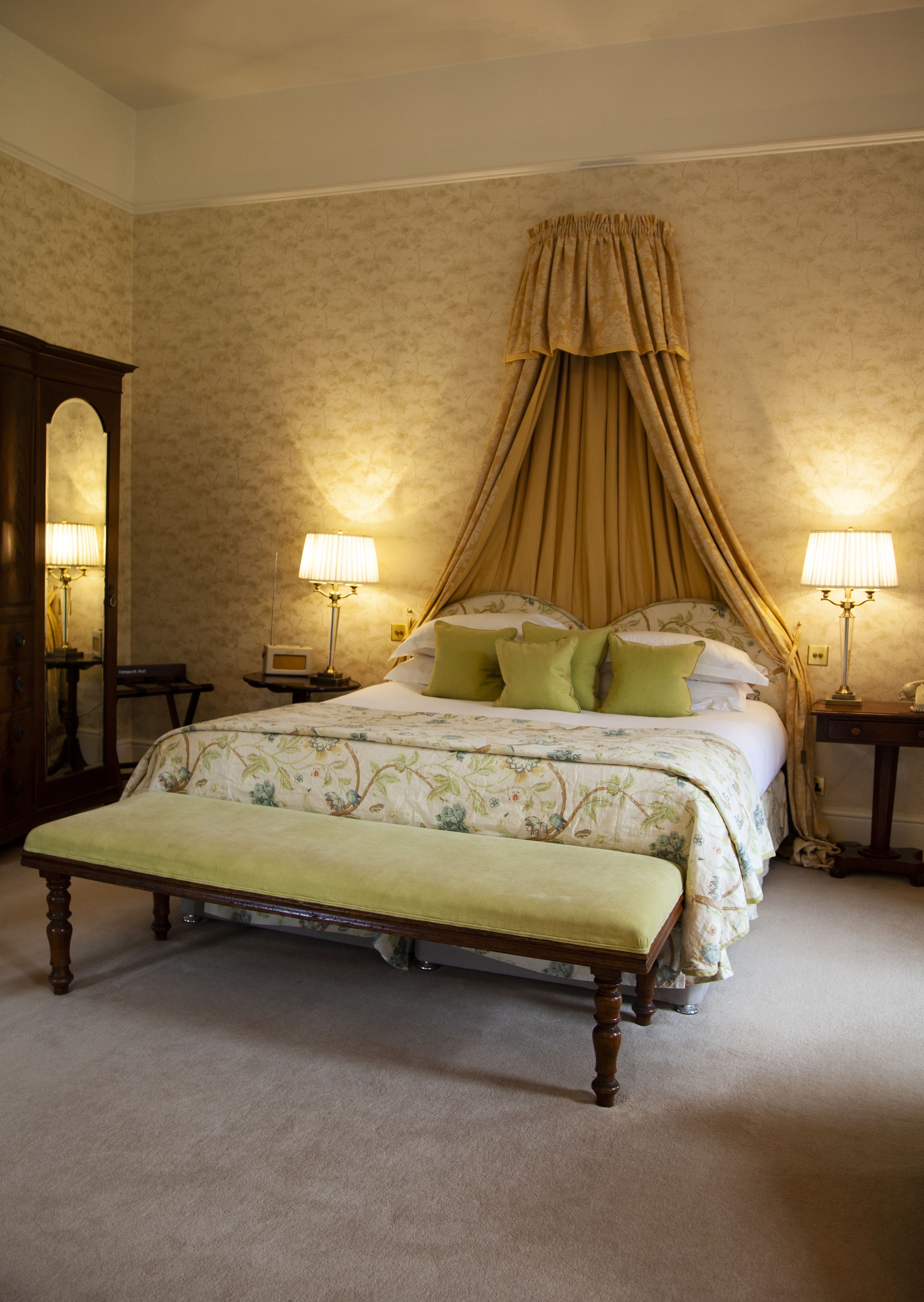 A bedroom with a canopy bed, two bedside lamps, a bench, and a mirror.