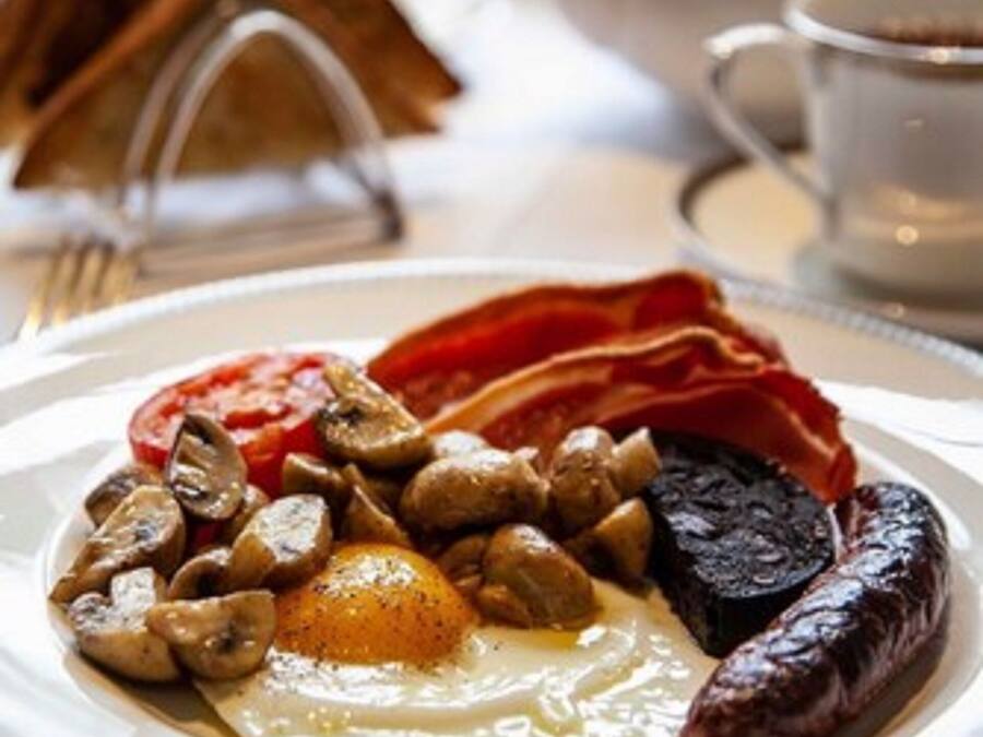 Un plato de desayuno con huevos, champiñones, tocino, salchicha y rodajas de tomate.