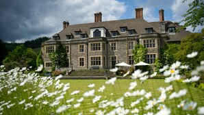 A large stone building with multiple windows and a well-maintained lawn with white flowers in the foreground.
