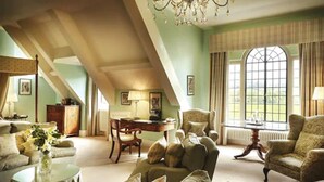 A spacious loft-style living room with high ceilings, a chandelier, and large windows offering a view of the outdoors. - Llangoed Hall (Brecon)