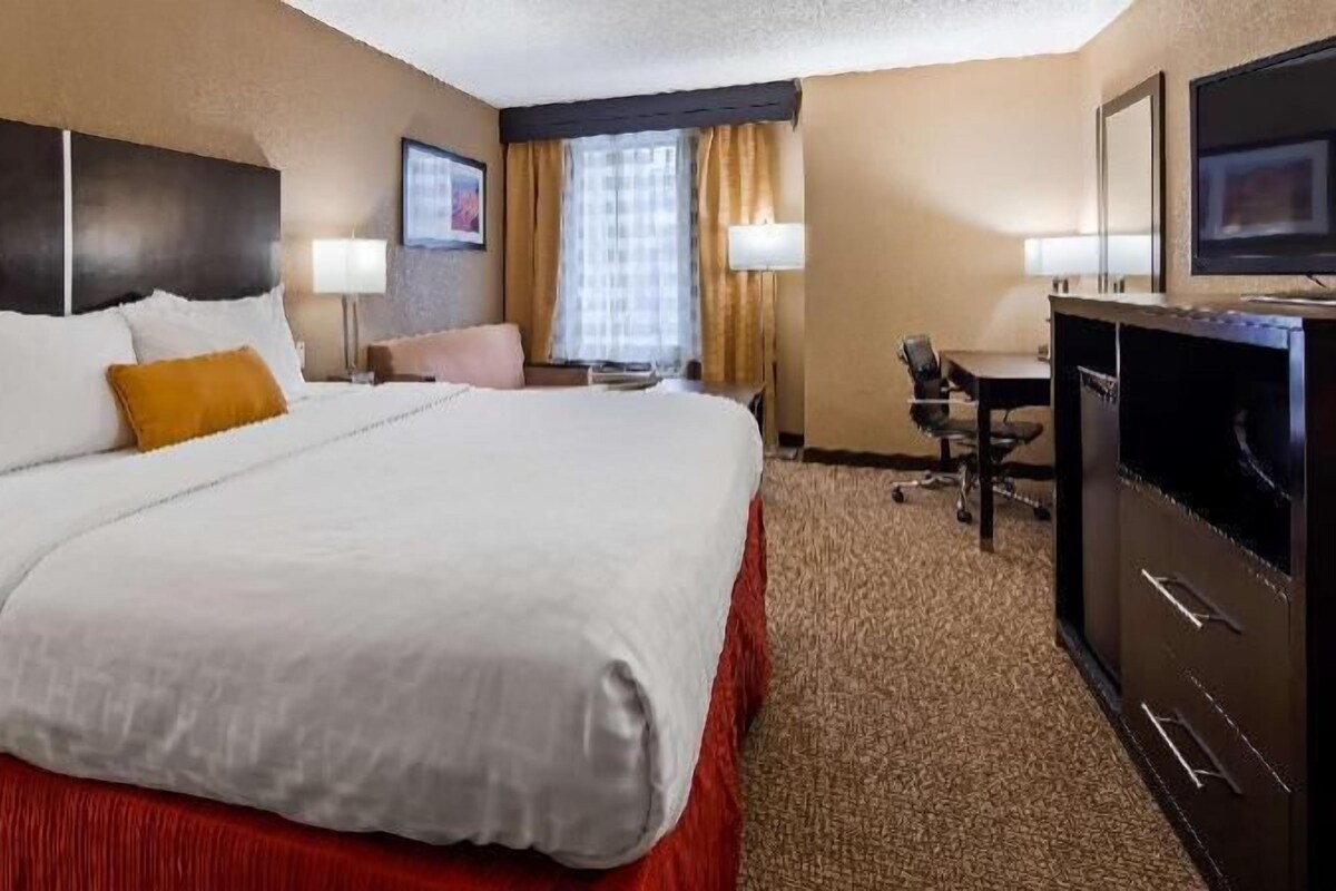 A hotel room with a large bed, a desk, a TV, and a window with curtains.