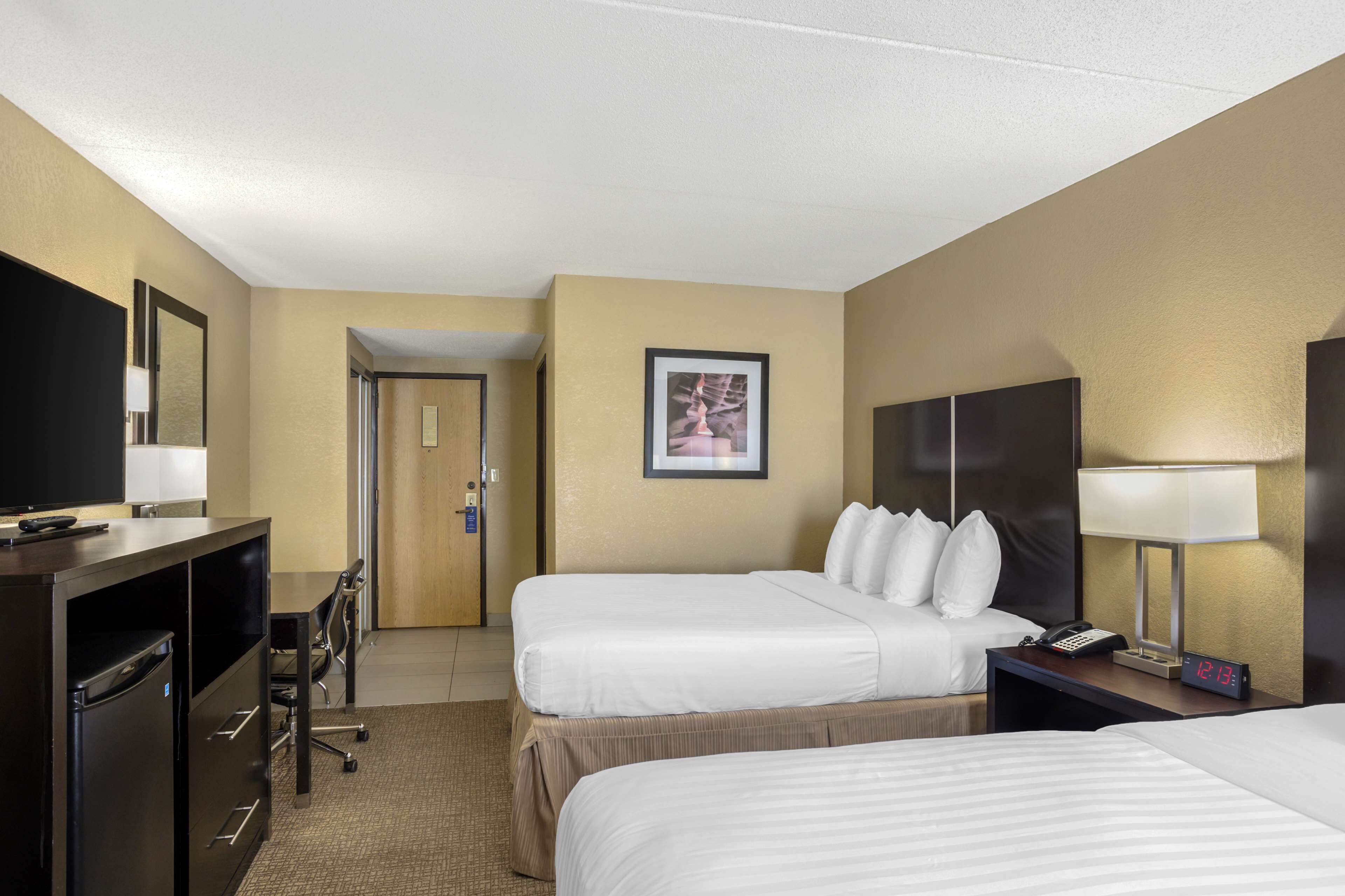 A hotel room with two beds, a desk with a computer, a TV, and a nightstand with a lamp and phone.