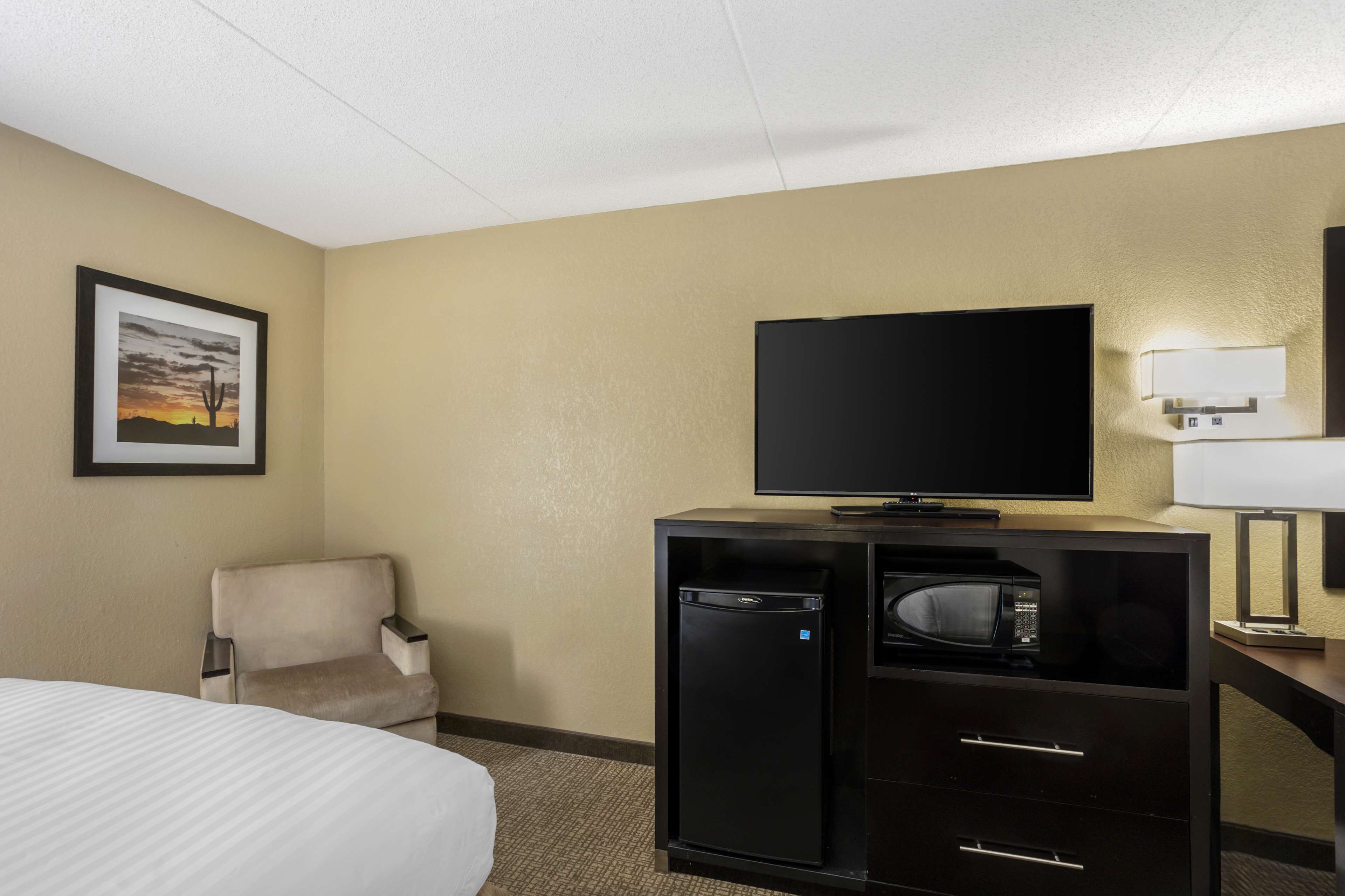 Habitación de hotel con una cama, un escritorio con televisor, un microondas y un refrigerador pequeño.