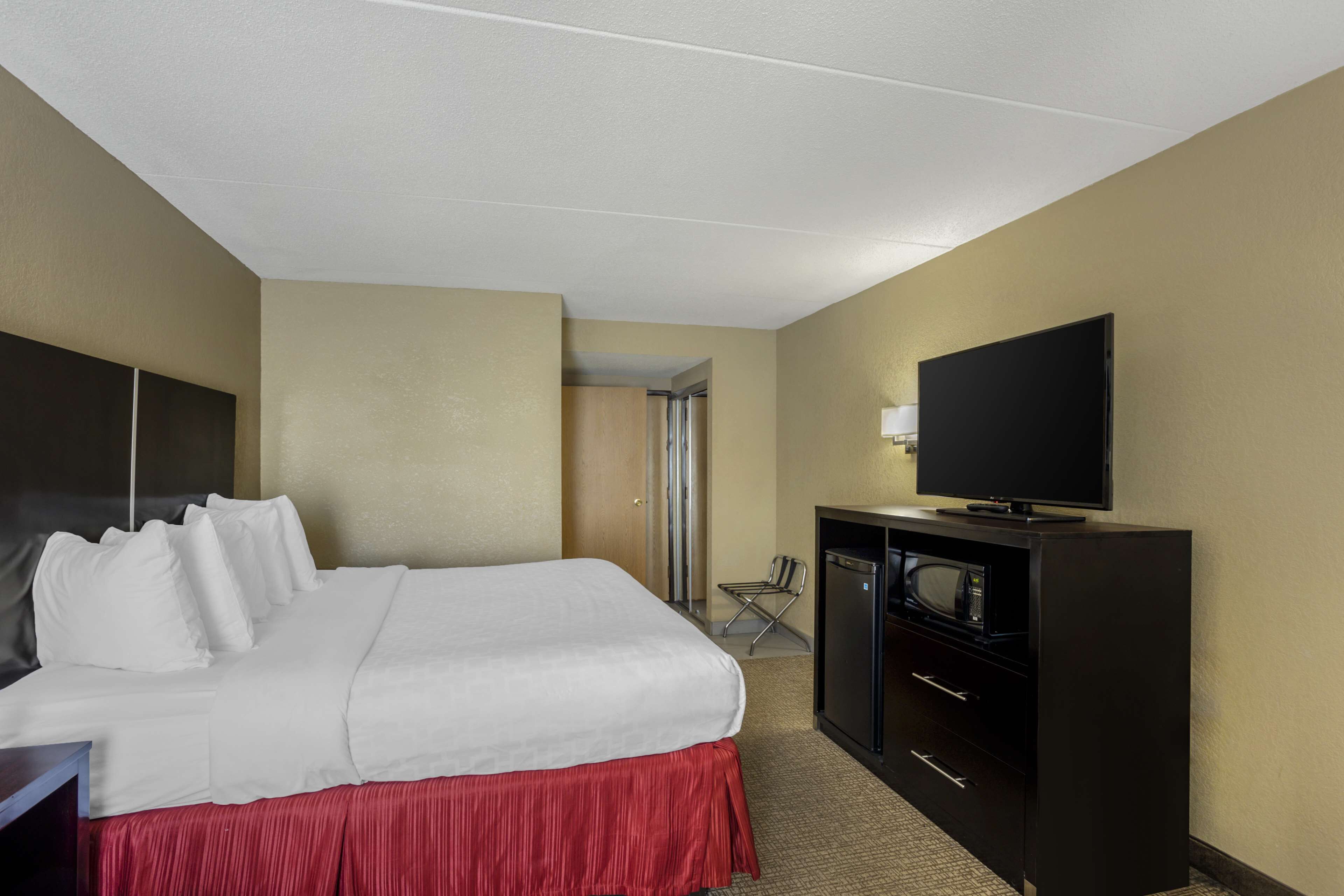 Una habitación de hotel con cama, televisión, escritorio con cajones y microondas.