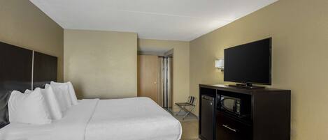 Una habitación de hotel con cama, televisión, escritorio con cajones y microondas.