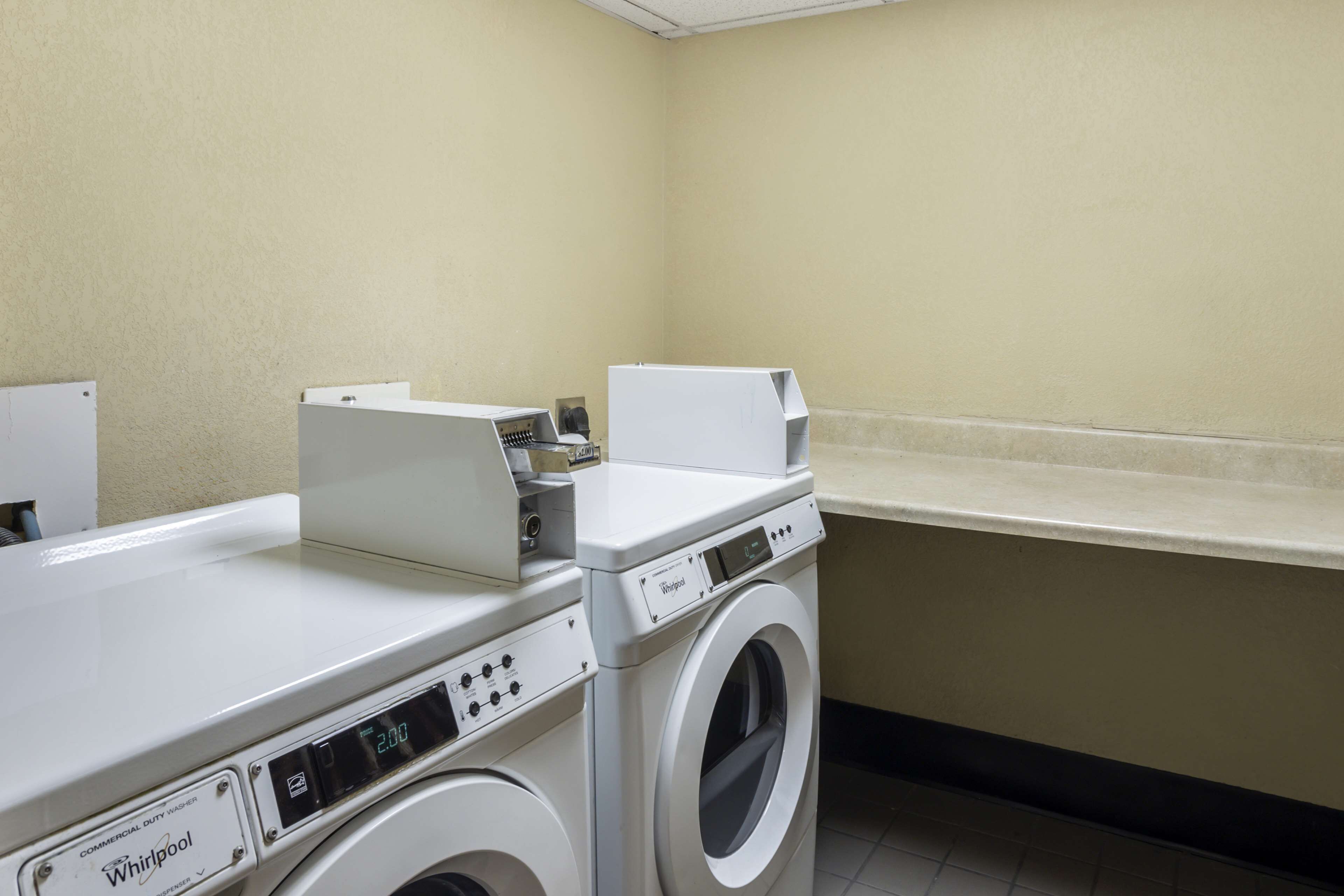 A laundry area with a front-loading Whirlpool washer and dryer, a countertop, and a wall-mounted dispenser.