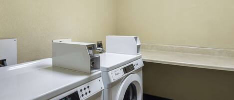A laundry area with a front-loading Whirlpool washer and dryer, a countertop, and a wall-mounted dispenser.