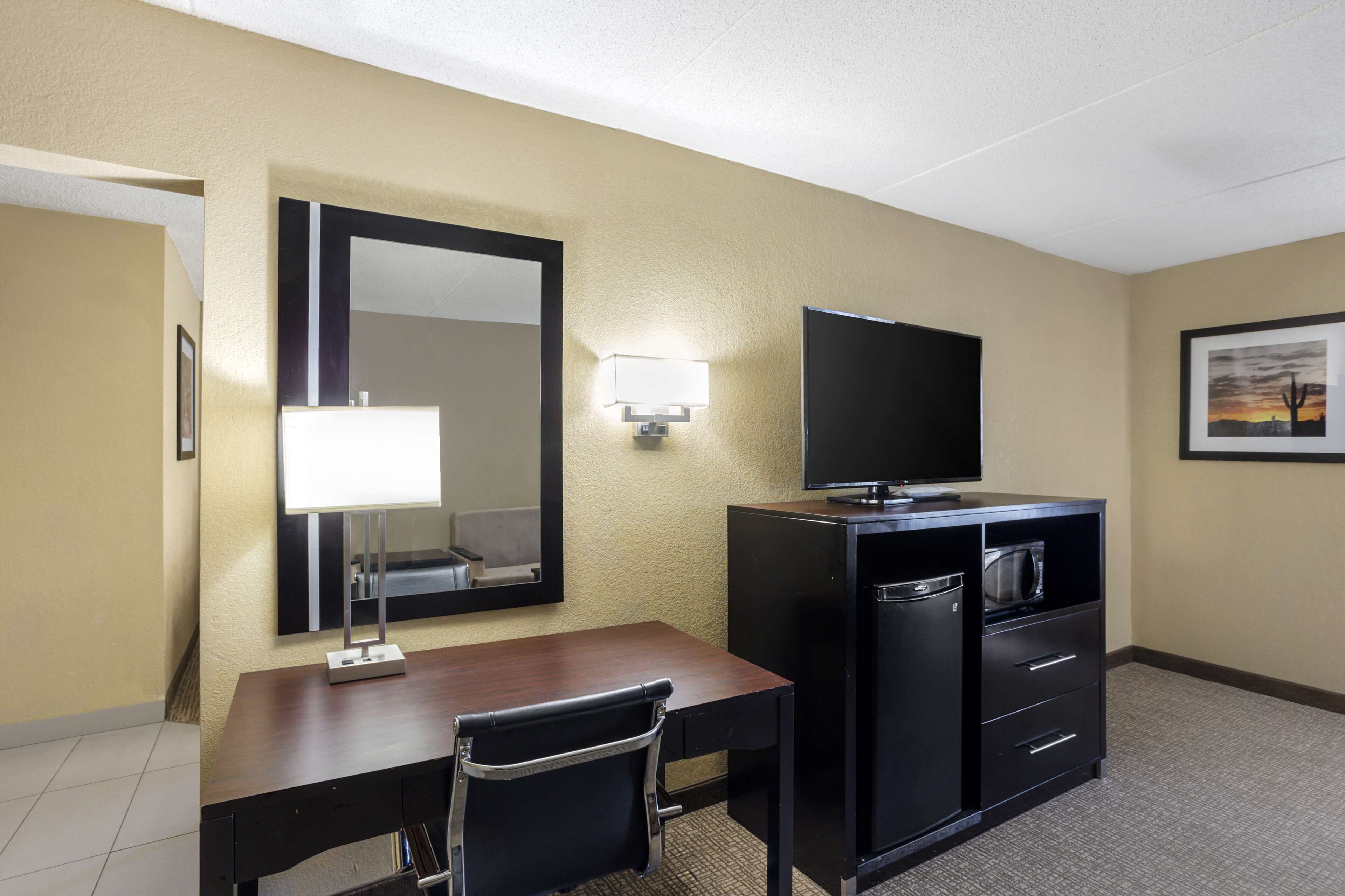 A hotel room with a desk, chair, television, and a minibar.