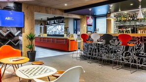 A modern bar area with a counter, bar stools, and a television screen. - ibis Toulouse Ponts Jumeaux (Toulouse)
