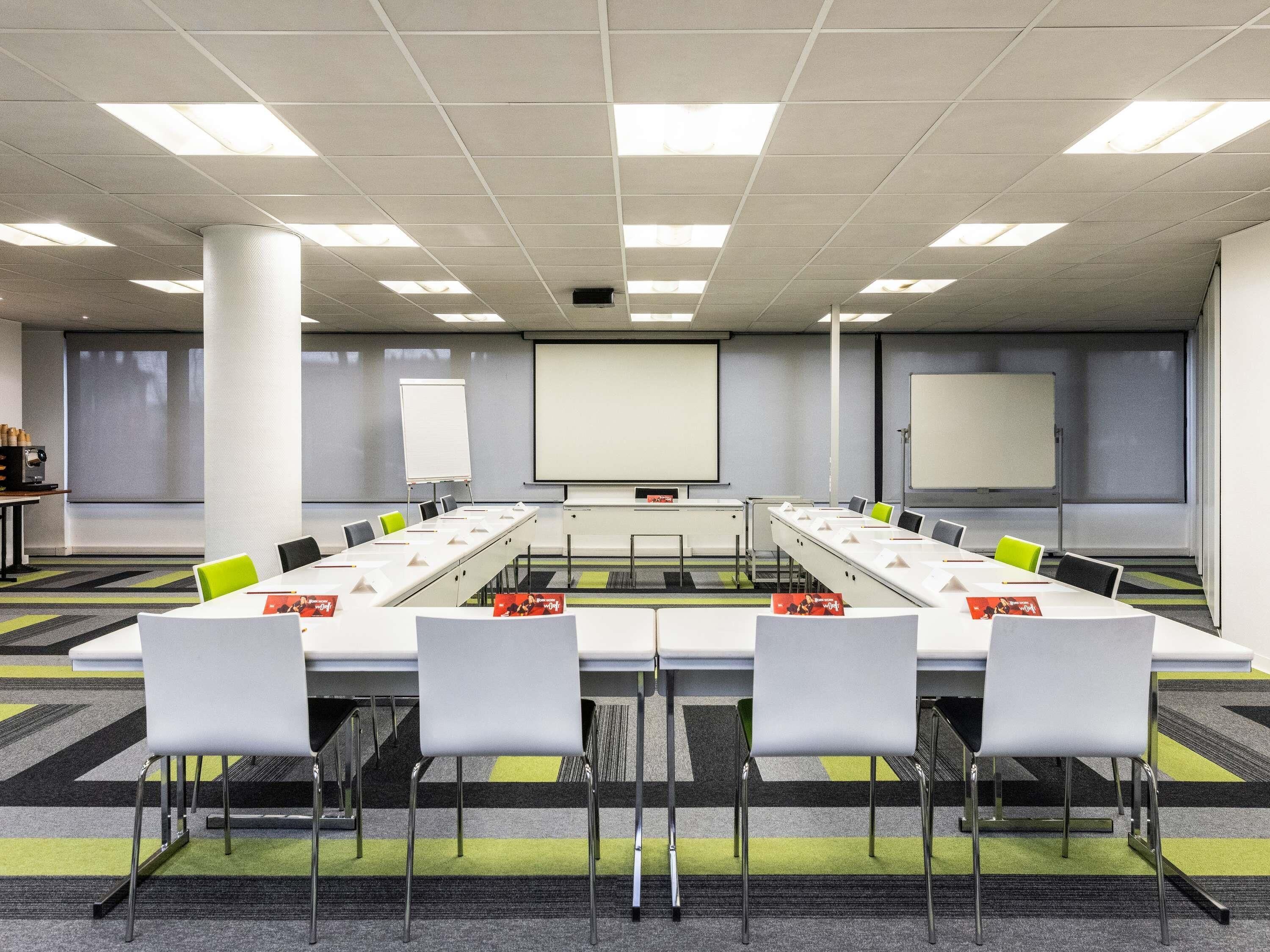 A conference room with a long table, chairs, a projector screen, and a whiteboard.