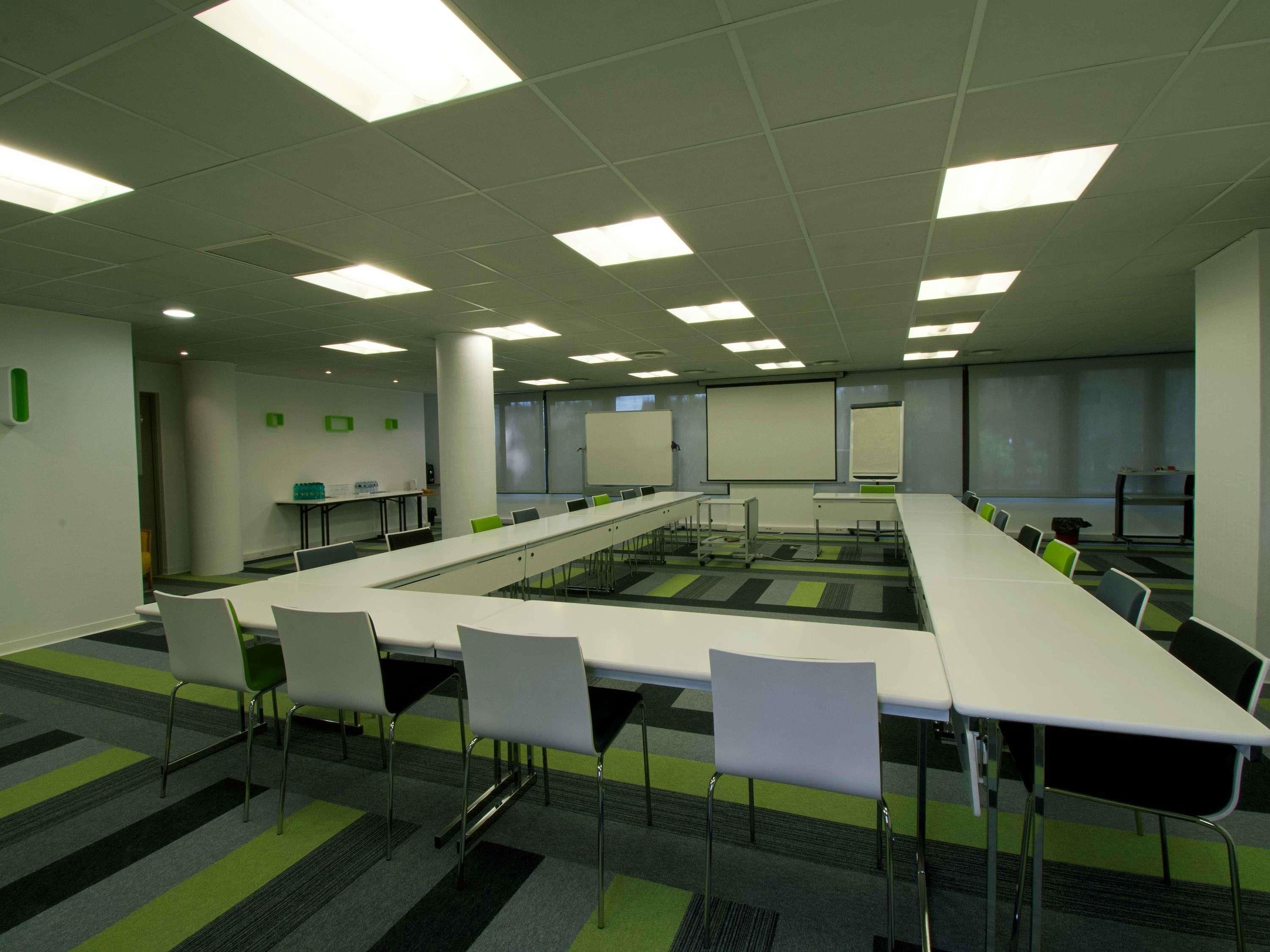 A conference room with a long table, chairs, a whiteboard, and a projector screen.