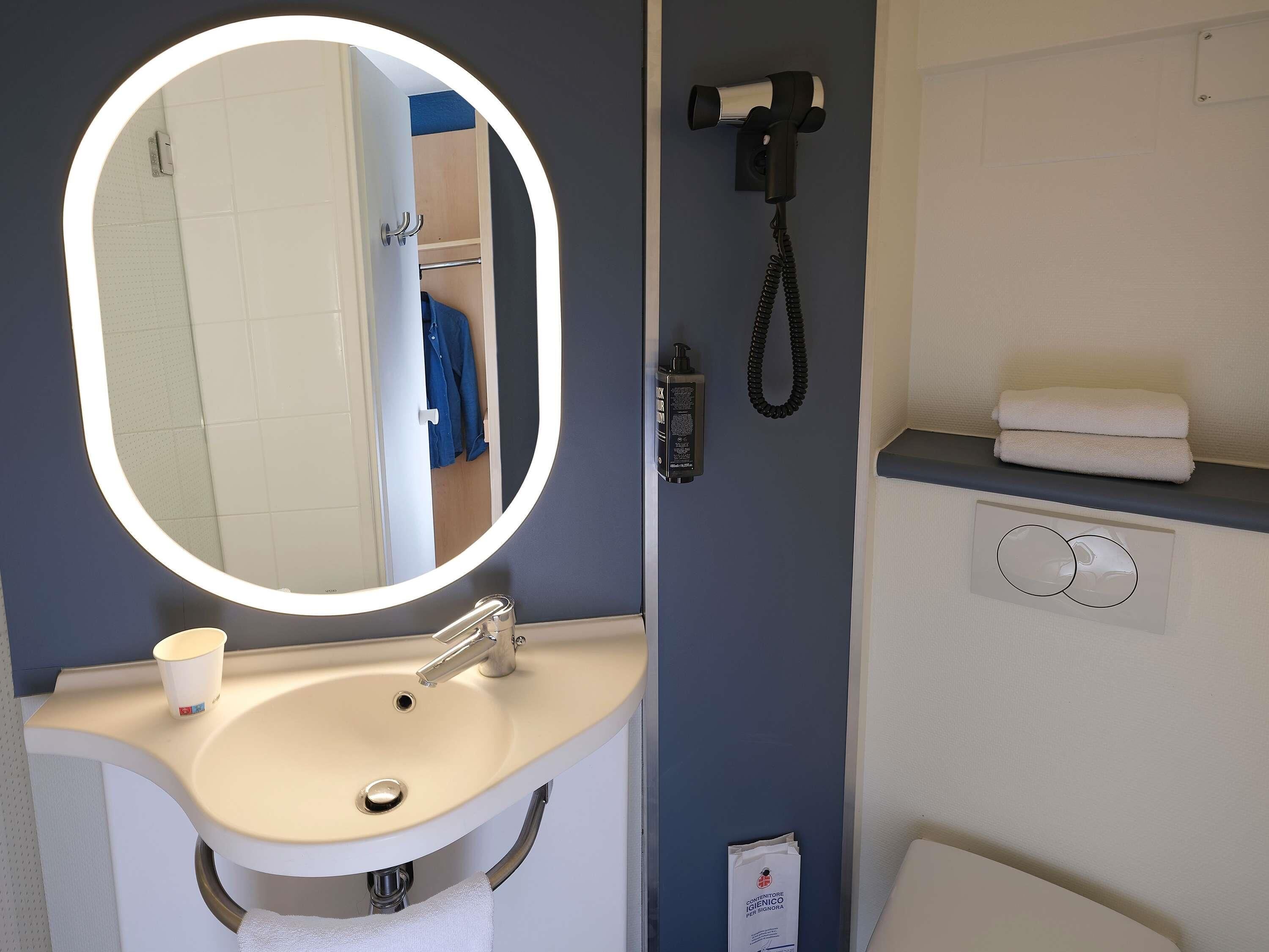 Un baño con un espejo redondo, lavamanos y perchero para toallas.