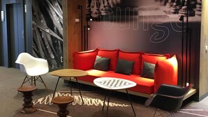 A modern lounge area with a red sofa, a white chair, and a small round table. - ibis Toulouse Ponts Jumeaux (Toulouse)