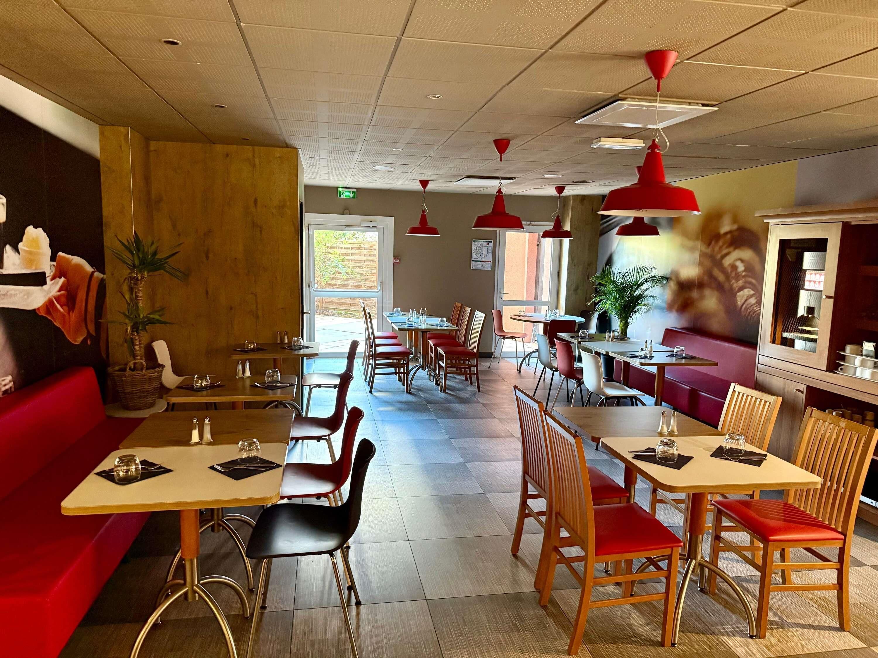 Interior de restaurante con mesas, sillas y lámparas colgantes rojas.