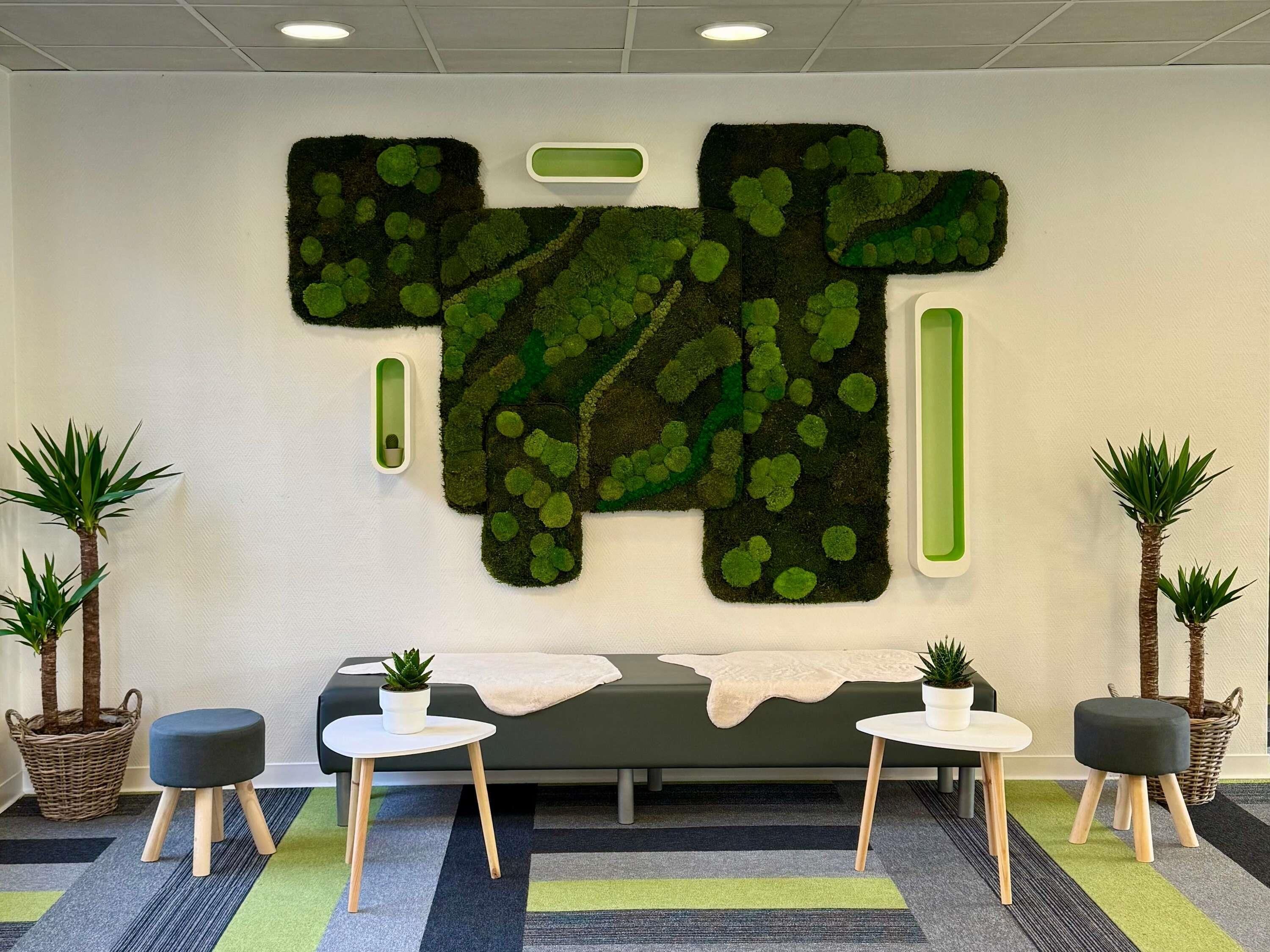 Un espace d’accueil agrémenté d’un mur végétal en mousse, d’un canapé, de deux petites tables et de plantes en pot.