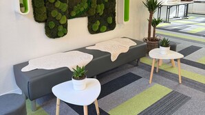 A modern lounge area with a green moss wall, a grey sofa, and two white tables with potted plants. - ibis Toulouse Ponts Jumeaux (Toulouse)