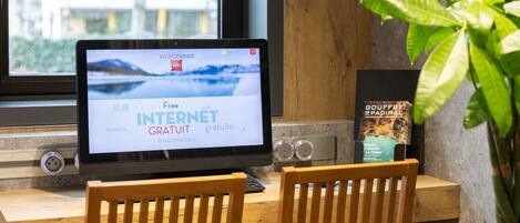 A laptop on a wooden desk with a plant beside it, a book titled 'Gouffre de Padiac,' and a window with a view of trees.