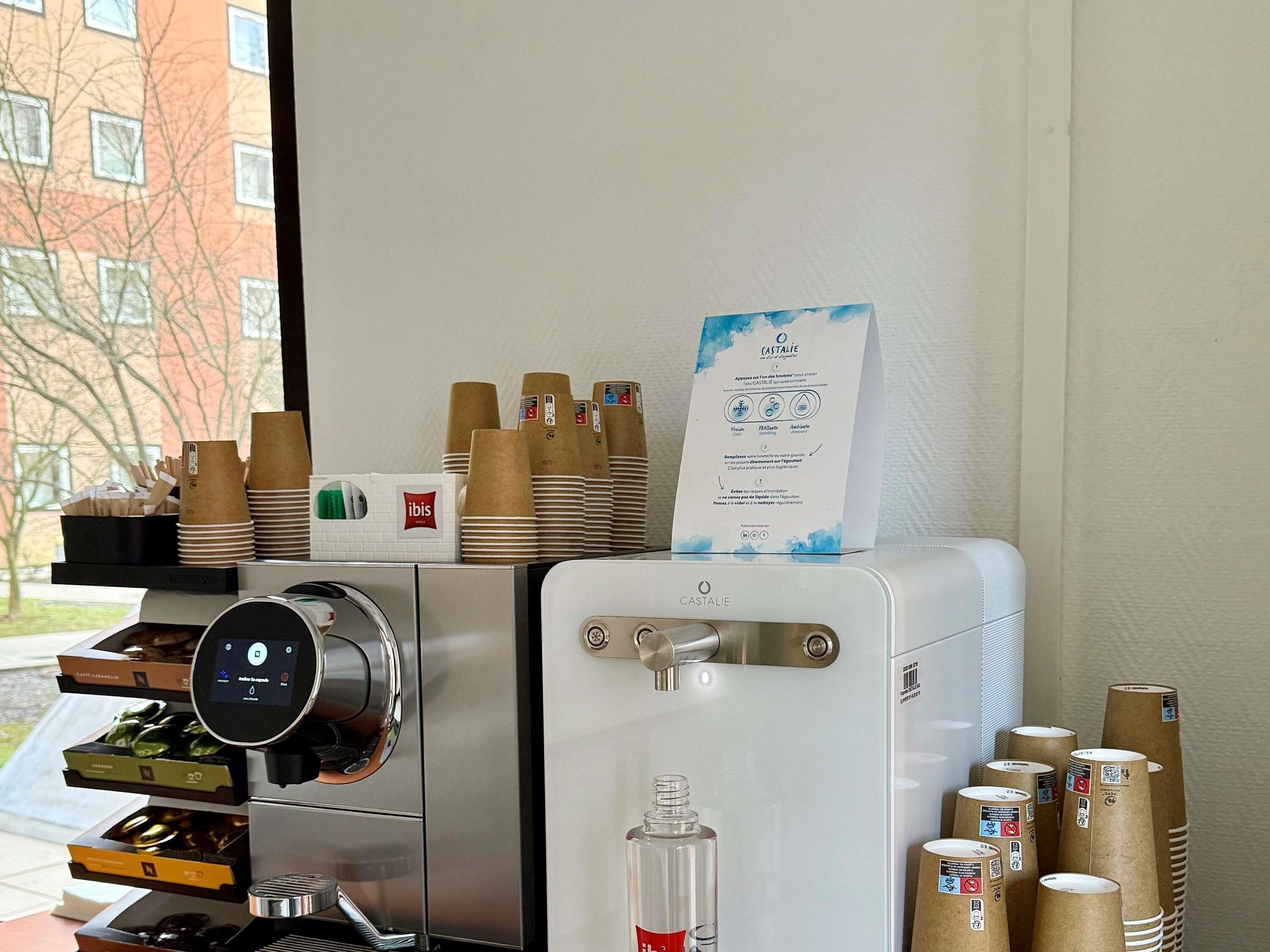 A coffee machine with a digital display, a water dispenser, and stacks of disposable cups.