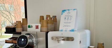 Una cafetera con pantalla digital, dispensador de agua y pilas de vasos desechables.