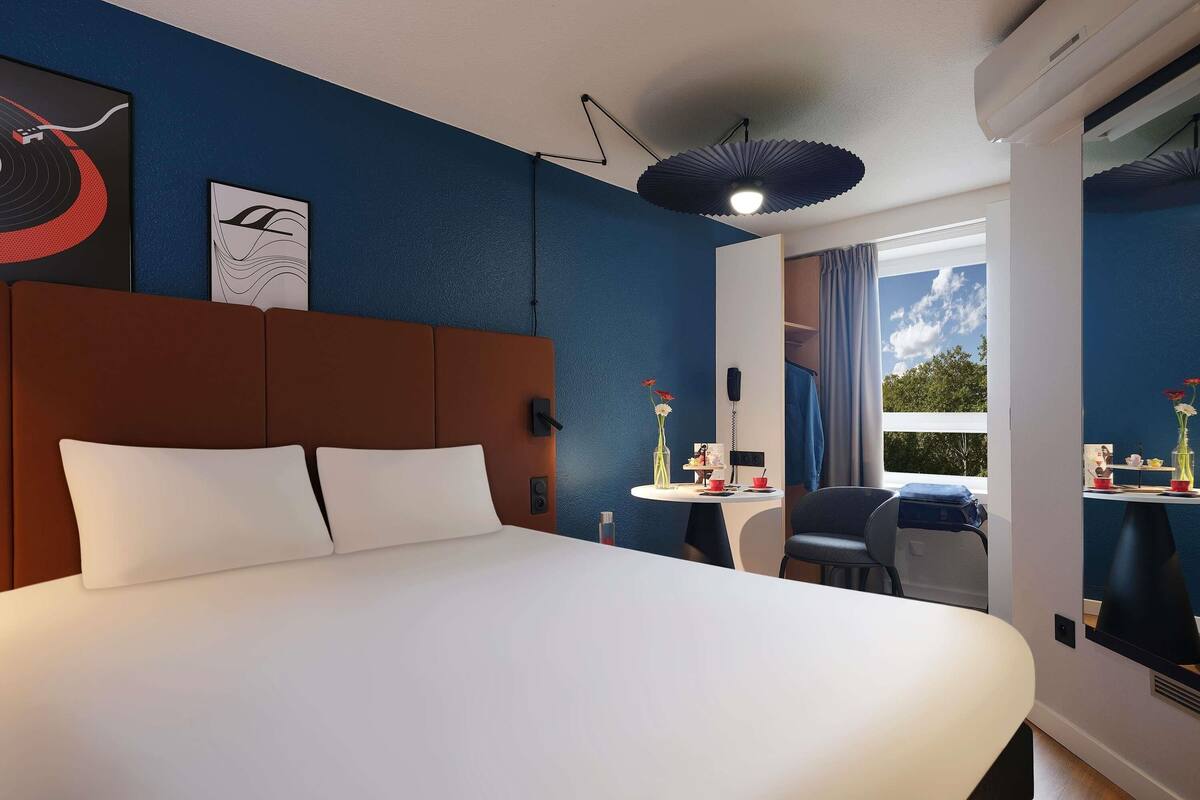 Ett hotellrum med en stor säng, ett skrivbord med en stol, ett fönster med utsikt och konstverk på väggarna.