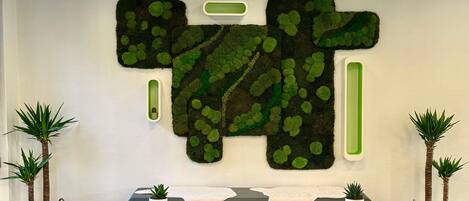 Un área de recepción con una gran obra de arte en la pared, dos zonas de estar con plantas y un mostrador de recepción.