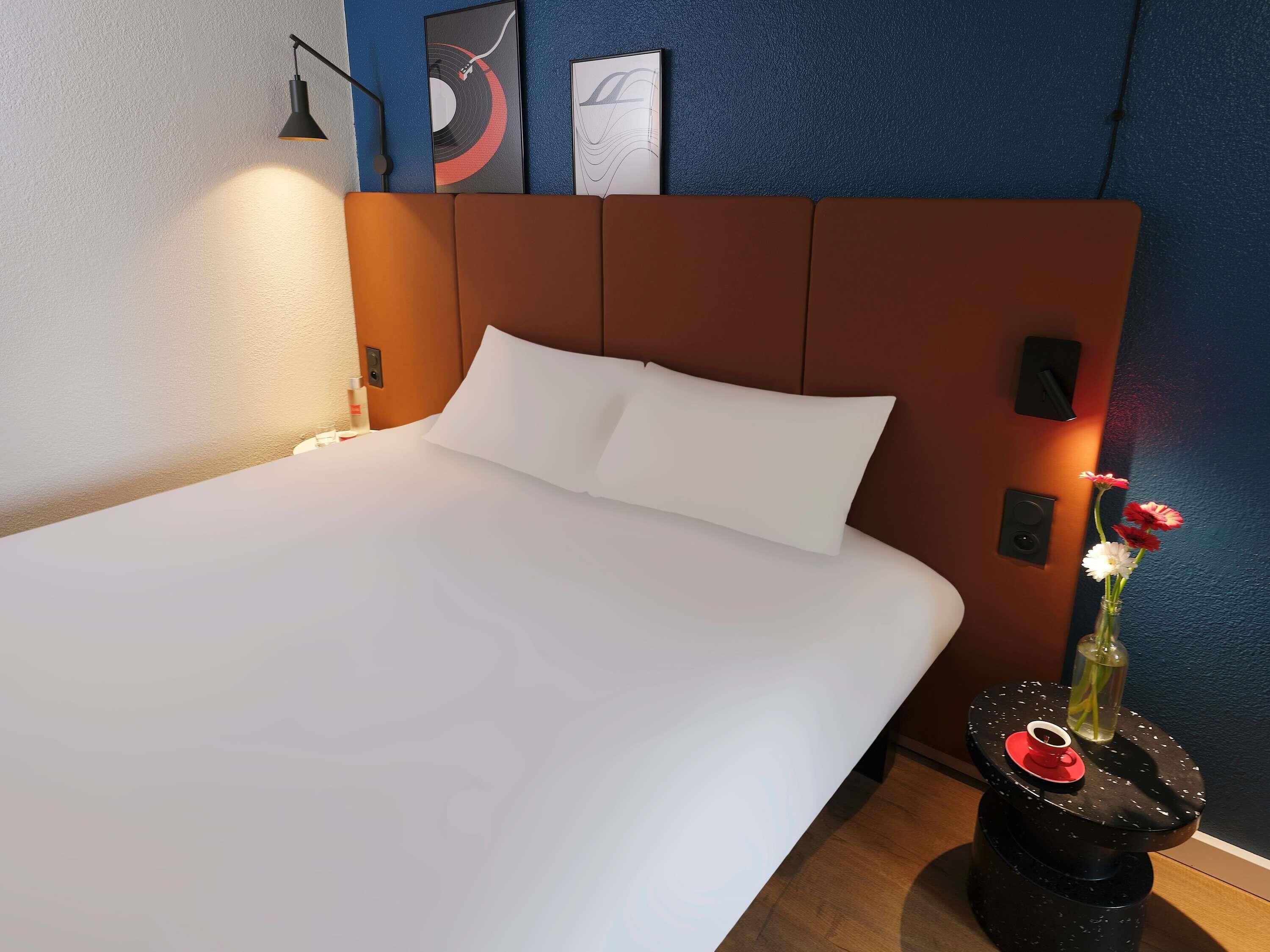 Ein ordentlich bezogenes Bett mit weißen Leinen, ein modernes Kopfbrett und ein kleiner Nachttisch mit einer Blumenvase.