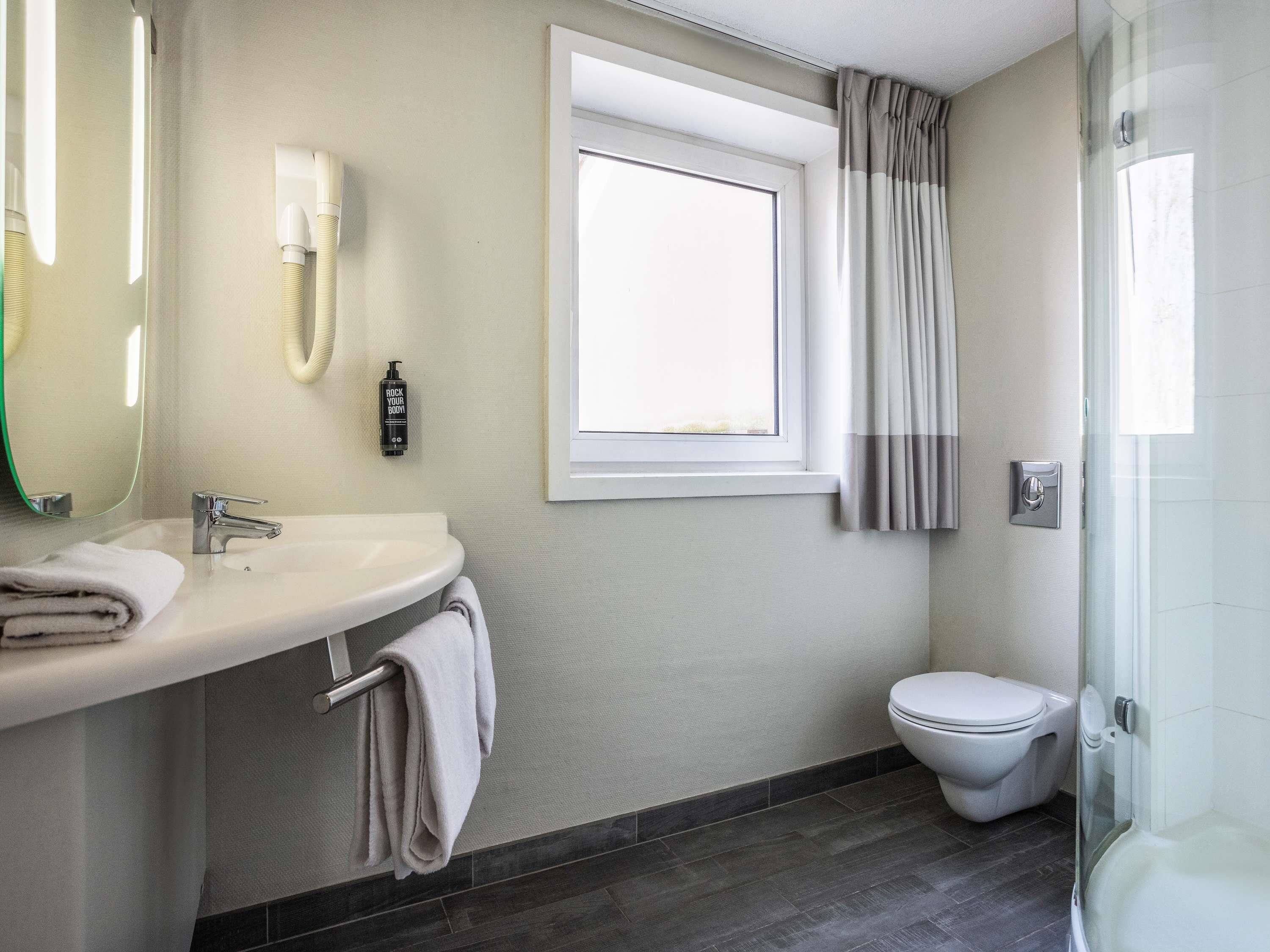 A modern bathroom with a white sink, a mirror, a towel rack, a toilet, and a shower area.