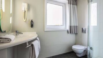 A modern bathroom with a white sink, a mirror, a towel rack, a toilet, and a shower area.
