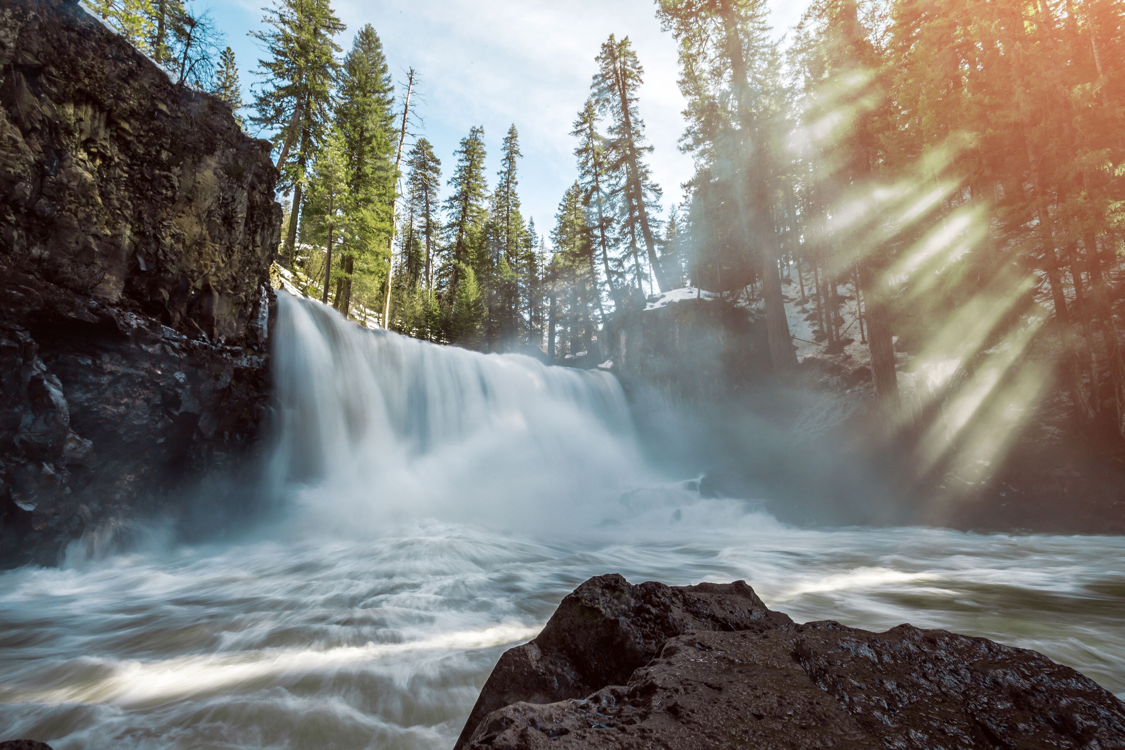 A waterfall surrounded by tall trees and rocky terrain.