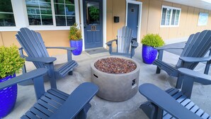 Eine Terrasse mit Adirondack-Stühlen, einem Beton-Feuerkorb und Blumentöpfen.