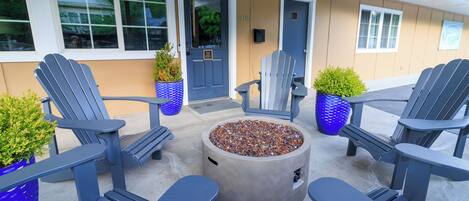 A patio with Adirondack chairs, a concrete fire pit, and potted plants.