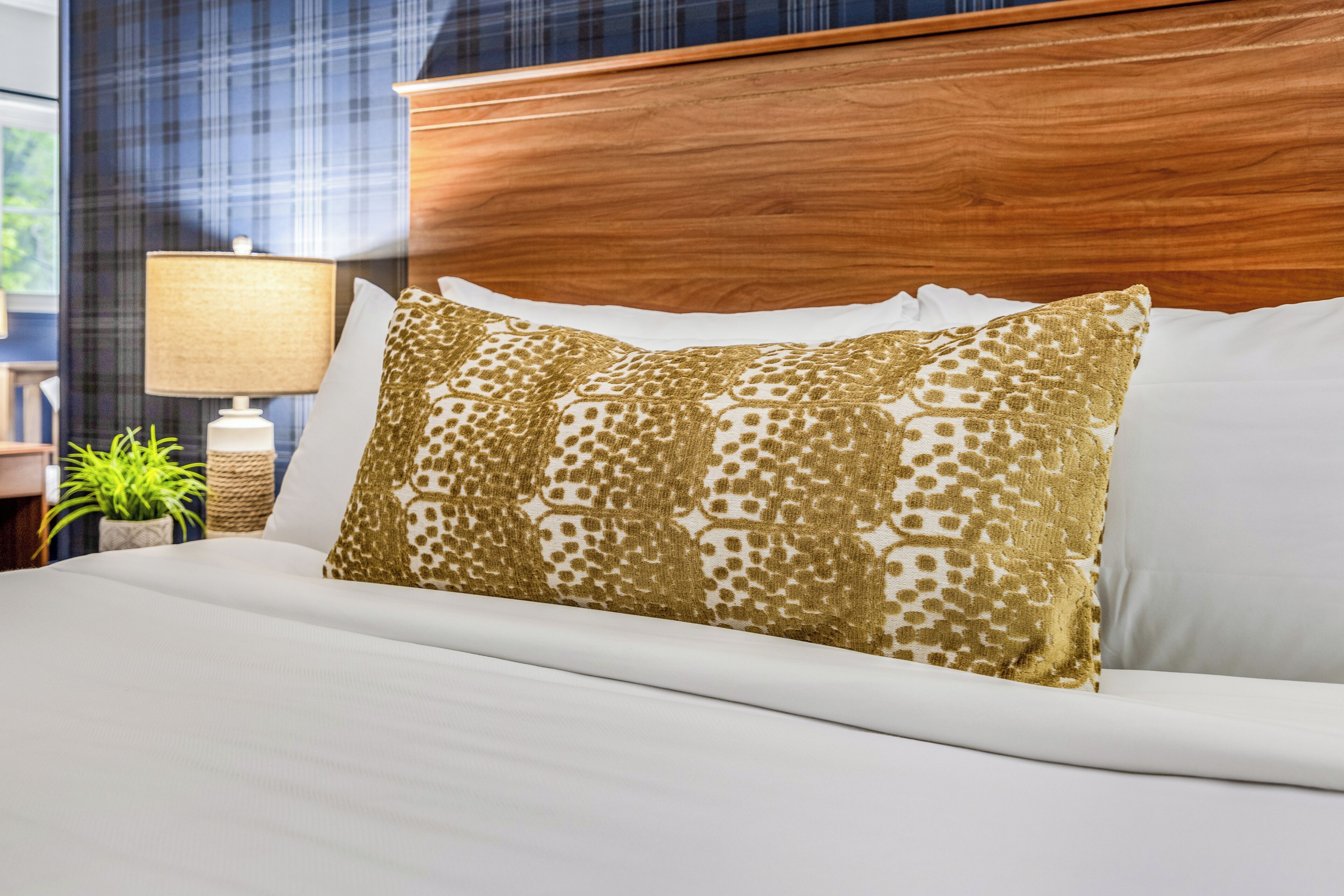 A neatly made bed with white linens and a patterned gold pillow.