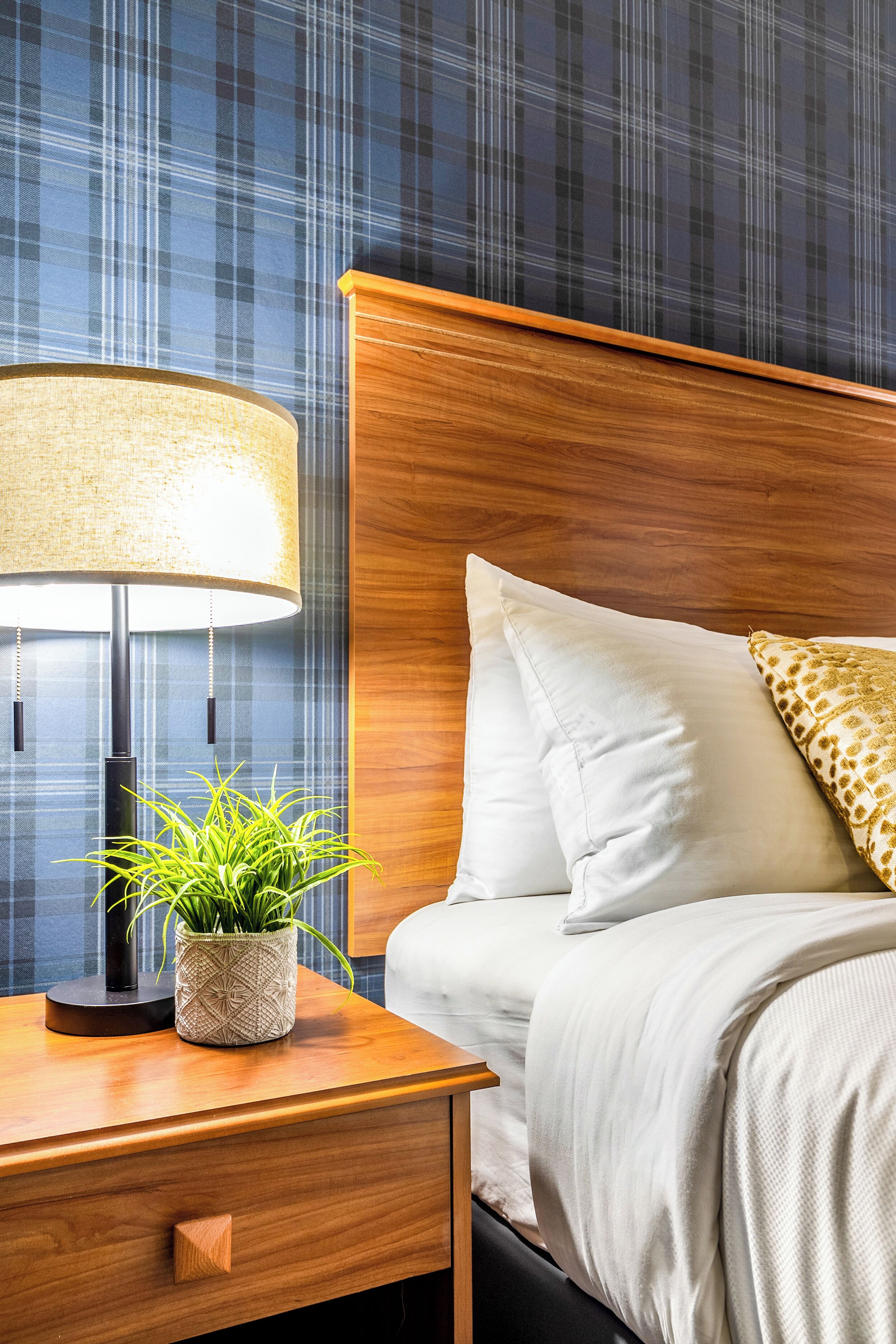 Un lit bien fait, avec du linge de lit blanc, une tête de lit en bois et un seul coussin décoratif.