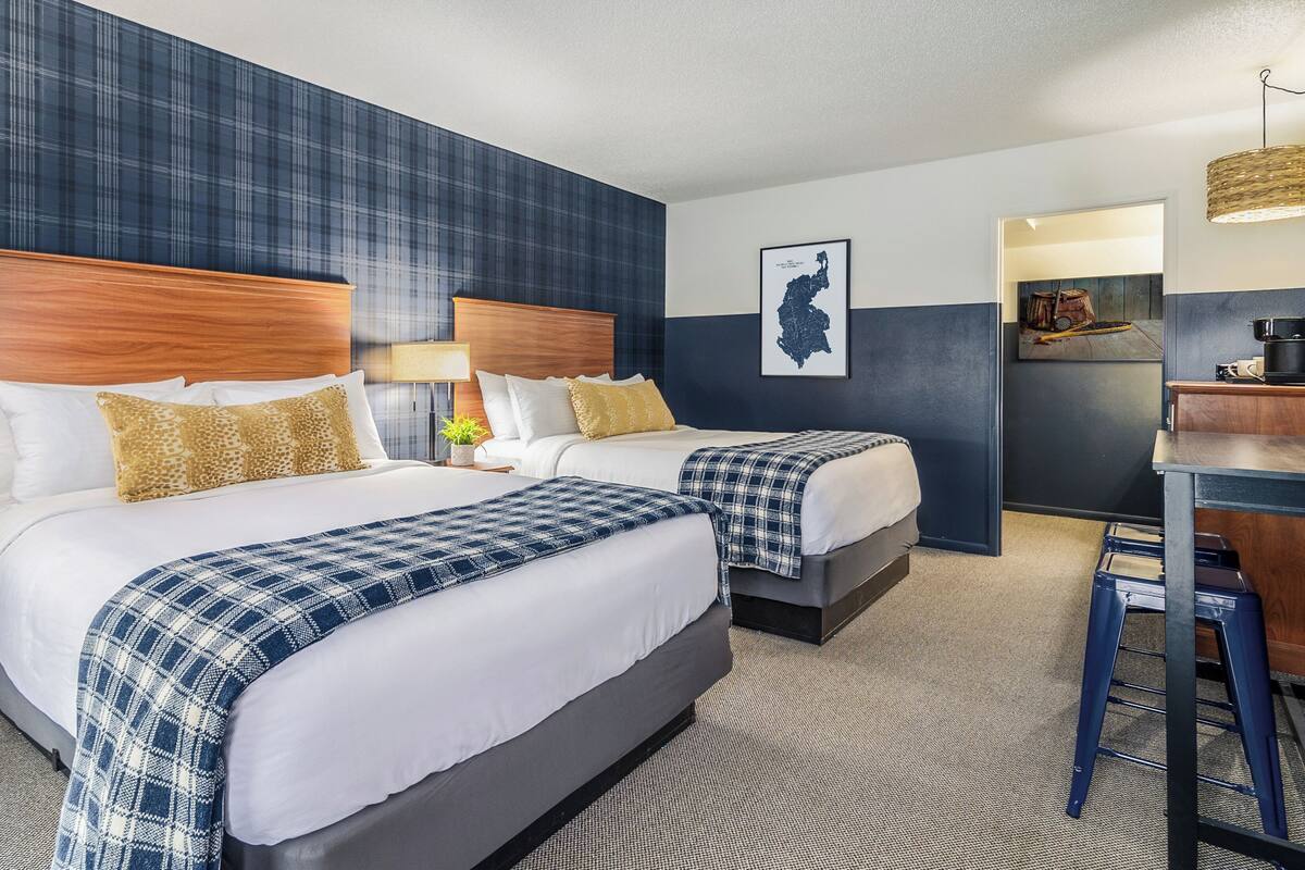 A hotel room with two beds, a desk, and a kitchenette.