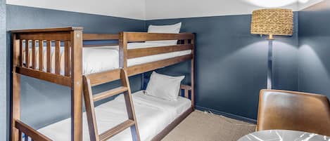 Een stapelbed met witte beddengoed, een geweven lamp en een stoel met een kussen met marmerprint.