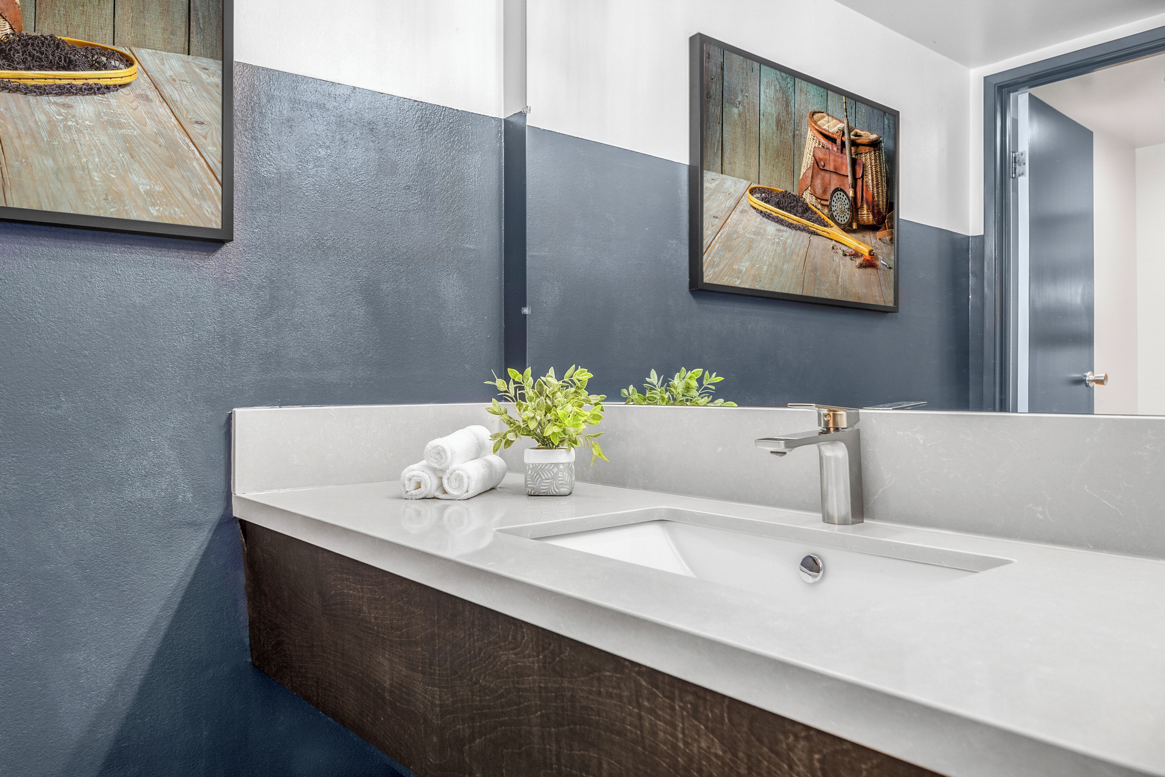 A modern bathroom with a white sink, dark wooden vanity, and two framed artworks on the walls.