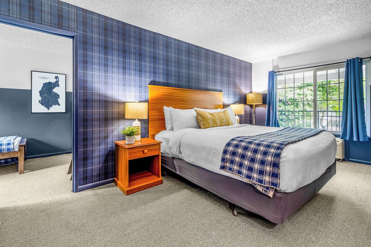A hotel room with a large bed, two bedside tables with lamps, a map on the wall, and a view of greenery through the window.